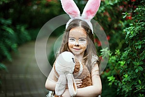 Children play with toy rabbit. Laughing child at Easter egg hunt with pet bunny. Little toddler girl playing with animal in the ga