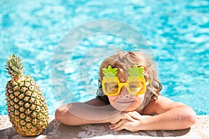 Children play in tropical resort. Little boy child having fun in swimming pool. Summer pineapple fruit.