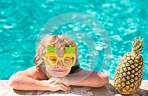 Children play in tropical resort. Little boy child having fun in swimming pool. Summer pineapple fruit.