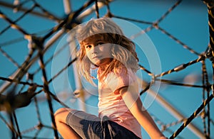 Children playground in urban park. Child climbing the net. Kids play and climb outdoors on sunny summer day.