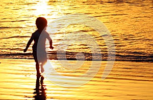 Children playing at the beach in Bali, Indonesia during a golden sunset. Ocean like gold.