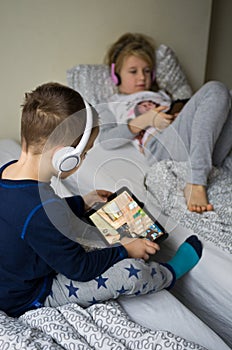 Children playing in bed with their tablets and phones