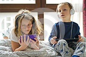 Children playing in bed with their tablets and phones