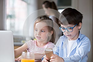 Children playing computer and smartphone while mother busy cooking breakfast