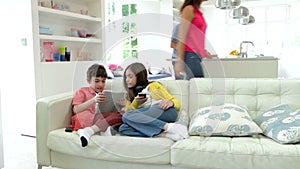 Children Playing With Digital Devices As Parents Make Meal