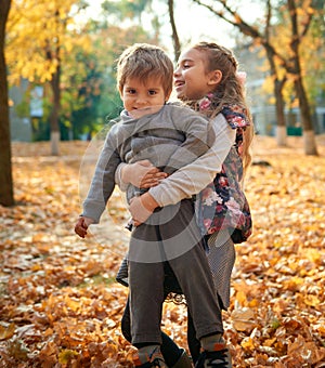 Children are playing on fallen leaves in autumn city park.