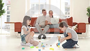 Children playing on floor while happy parents relax on couch