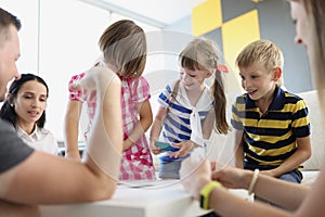 Children playing fun card game with adults, brothers and sisters having fun at home with parents