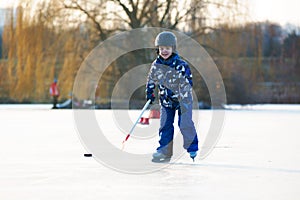 Children, playing hockey and skating in the park on frozen lake, wintertime on sunset