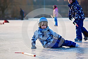 Children, playing hockey and skating in the park on frozen lake, wintertime on sunset