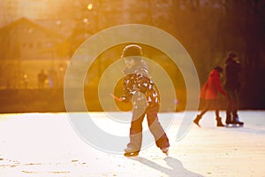 Children, playing hockey and skating in the park on frozen lake, wintertime on sunset