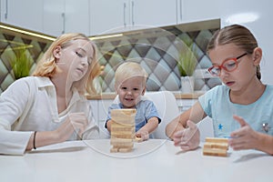 Children playing Jenga tower to remove wooden blocks at home. two girls and boy having fun together - board game and kids leisure