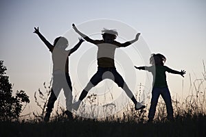 Children playing jumping on summer sunset meadow silhouetted