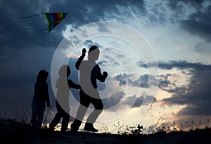 Children playing kite on summer sunset meadow silhouetted