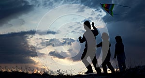 Children playing kite on summer sunset meadow silhouetted