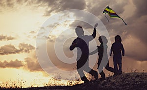 Children playing with kite on summer sunset meadow silhouetted