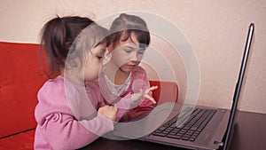 Children playing in the laptop. Two little girls are printed on a laptop. Two sisters sitting on the orange couch looking at a lap