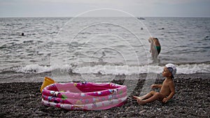 Children playing near inflatable baby pool. Boy sitting on the pebbles