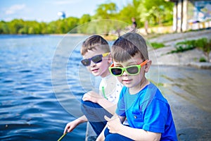 Children playing outdoors in nature: sitting on lake or river shore touching sand in clear water on warm summer or spring day.