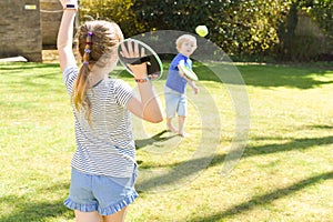 Children playing outside a brother and sister play a ball game in a garden