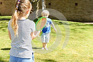 Children playing outside a brother and sister play a ball game in a garden