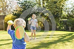 Children playing outside a brother and sister play a ball game in a garden