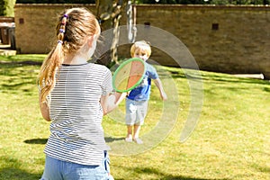 Children playing outside a brother and sister play a ball game in a garden