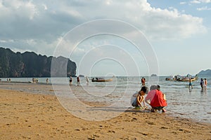 Children playing sand and some people walking and relaxing at Ao Nang beach before the sunset