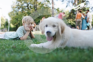 Children playing with a small puppy at a family garden party. Portrait of little boy lying on grass with Golden