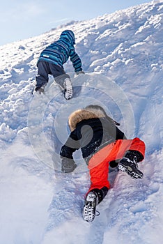 Children playing in snow. One Asian boy and girl in ski-wear climbing in winter