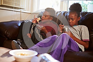 Children With Poor Diet Eating Meal On Sofa At Home