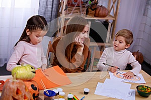 Children prepare Halloween decorations, paint and carve. A loving mother next to them at the table helps them with this