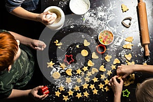 Children prepare star-shaped birthday cookies on a dark kitchen table. Family joint activity in the kitchen at home. View from