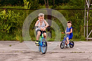 Children preschoolers ride a two-wheeled bike on the paved area in the summer. Children and sports