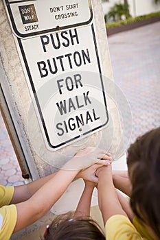 Children pressing a button at traffic lights on pedestrian crossing and having fun on a sunny summer day. Teamwork
