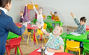 Children pull their hands to answer teacher question in the school class