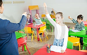 Children pull their hands to answer teacher question in the school class