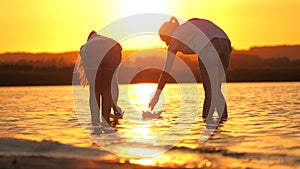 Children put a paper boat into water. Girls play with paper boats. Child`s hands launches a boat in park into river