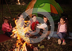 Children reading book with flashlight outdoors. Summer camp