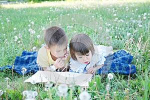 Children reading book lying on stomach outdoor among dandelion in park, cute children education and development. Back to school co