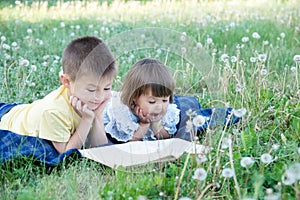 Children reading book in park lying on stomach outdoor among dandelion in park, cute children education and development