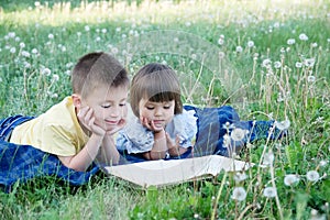Children reading book in park lying on stomach outdoor among dandelion in park, cute children education and development