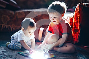 Children reading a book sitting together on floor at home. brother and babysister smiling having fun with book together. Boy and