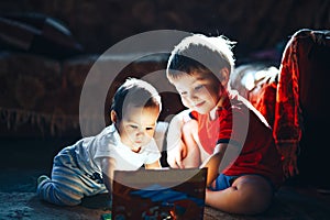 Children reading a book sitting together on floor at home. brother and babysister smiling having fun with book together. Boy and