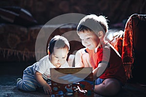 Children reading a book sitting together on floor at home. brother and babysister smiling having fun with book together. Boy and