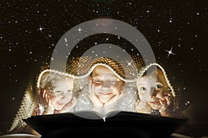 Children reading a book under a blanket with light