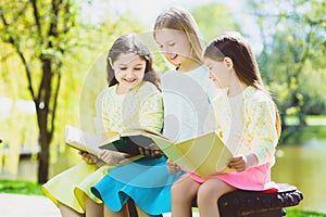 Children reading books at park. Girls sitting against trees and lake outdoor