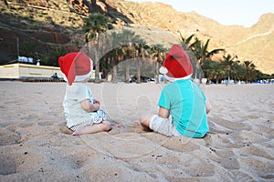 Children in red santa hats have fun on ocean sand beach