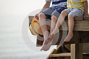 Children relax by the sea sitting on the edge of a wooden jetty with sea background. Sunny joyful summer day