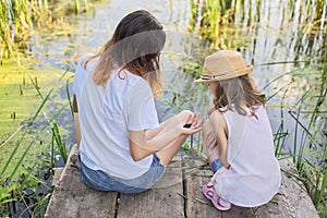 Children resting near the water on summer day, playing with water snails, back view